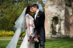 couple kissing at babington house wedding with floral bouquet by passion and a lace wedding gown